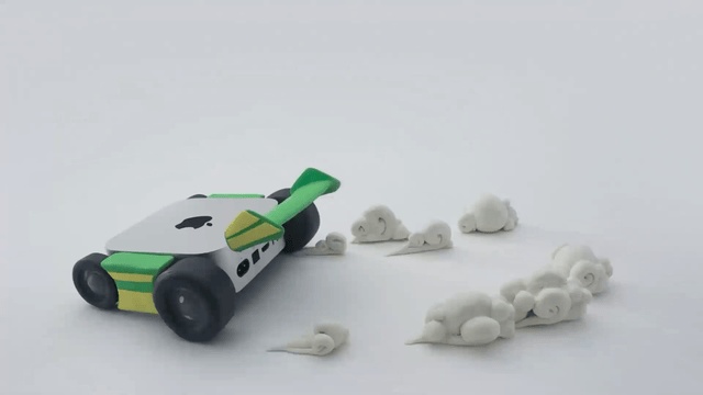 Frame real da animação oficial: Mac mini transformado em carro com rodas verdes e nuvens de massinha.